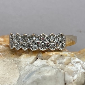 Puede incluir: Un anillo de banda de plata con una fila de pequeños diamantes engastados en un diseño festoneado.