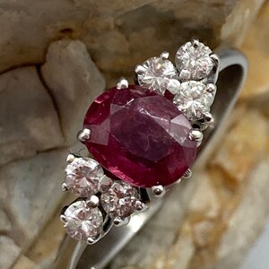 May include: A silver ring with a large oval ruby gemstone surrounded by smaller round diamonds.