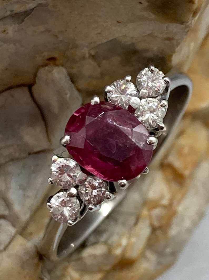 May include: A silver ring with a large oval ruby gemstone surrounded by smaller round diamonds.