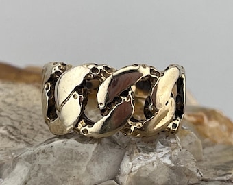 May include: A gold-colored ring with a chain link design. The ring has a textured surface and is displayed on a light-colored stone. The links are interlocked, creating a bold and stylish look. This ring is a piece of jewelry.