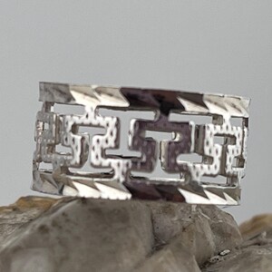 May include: A silver ring featuring a geometric design. The ring is crafted from smooth metal and has a polished finish.