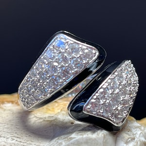 Può includere: Un anello d'argento con smalto nero e pietre di zircone cubico trasparenti. L'anello è progettato in uno stile unico e aperto.