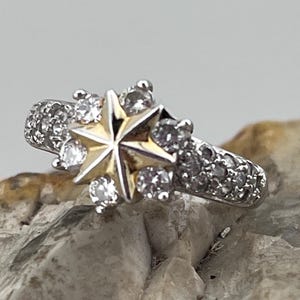 Peut inclure: Une bague en argent avec une pierre centrale en forme d'étoile dorée entourée de petites pierres claires.