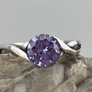 Peut inclure: Une bague en argent avec une bande torsadée et une grande pierre précieuse ronde de couleur violette.