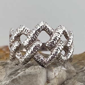 May include: A silver ring with a woven design. The ring is made of textured metal and has a unique, intricate pattern.
