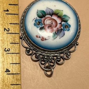 Peut inclure: Un pendentif en argent avec un cam&eacute;e en porcelaine bleu et blanc repr&eacute;sentant un motif floral peint &agrave; la main avec une rose rose et des fleurs bleues.