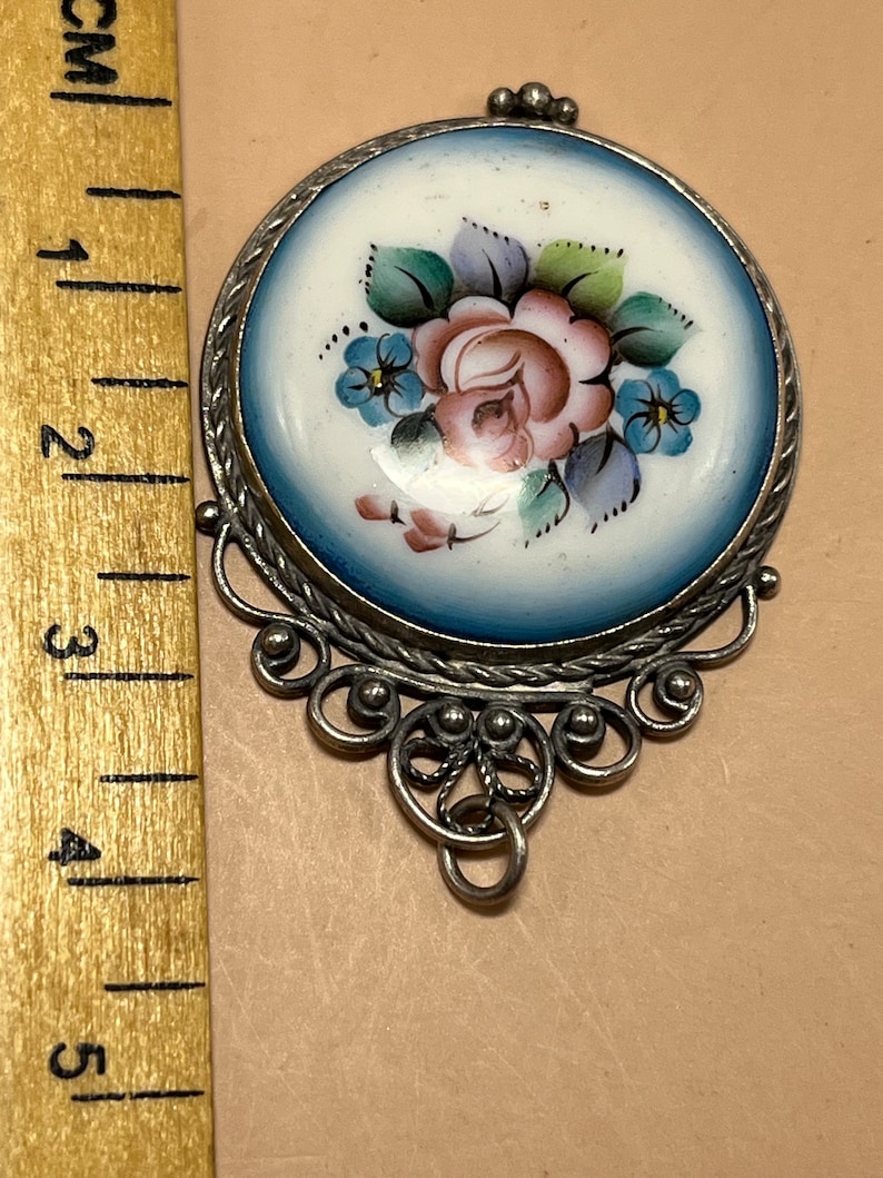 Peut inclure: Un pendentif en argent avec un cam&eacute;e en porcelaine bleu et blanc repr&eacute;sentant un motif floral peint &agrave; la main avec une rose rose et des fleurs bleues.