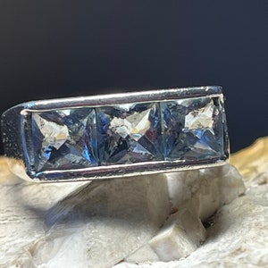 May include: A silver ring with three square-shaped blue gemstones set in a row.