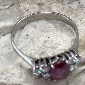 May include: A silver ring with a large red ruby gemstone surrounded by smaller diamonds.