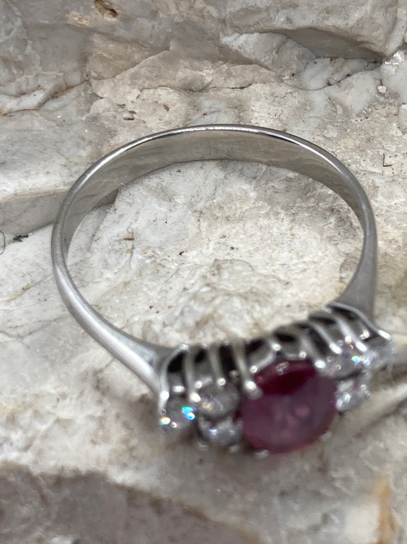 May include: A silver ring with a large red ruby gemstone surrounded by smaller diamonds.