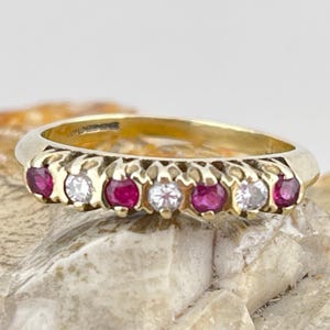 以下が含まれることがあります： 交互に赤いルビーと透明なダイヤモンドが並んだゴールドのバンドリング。リングは繊細で複雑なデザインです。