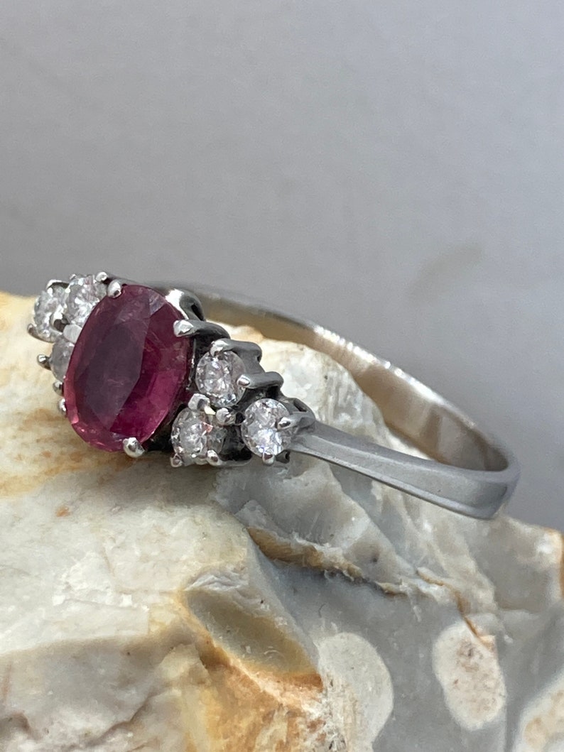 May include: A silver ring with a pink oval gemstone surrounded by smaller clear gemstones.