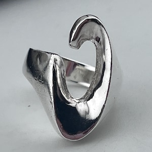 May include: A silver-colored ring with a unique, open design. The ring features a curved, wave-like shape that wraps around the finger. The polished metal reflects light, highlighting the ring's smooth surface and modern aesthetic.