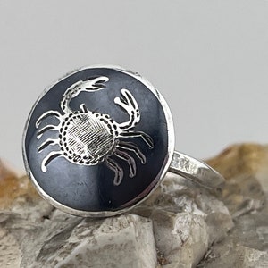 Peut inclure: Une bague en argent avec un centre en émail noir représentant un crabe argenté détaillé.