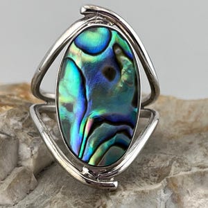 Peut inclure: Bague en argent ornée d'une coquille d'ormeau ovale. La coquille irisée présente des nuances de bleu, de vert et de violet. La bague a un design unique avec un anneau argenté incurvé.