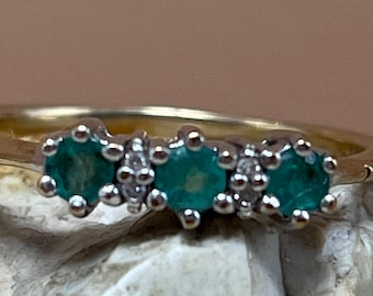 May include: A gold band ring with three green gemstones and small white diamonds set in the band.