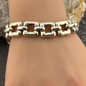 May include: A silver bracelet featuring a series of rectangular links. The bracelet is displayed on a wrist, highlighting its design and metallic shine. The links are connected, creating a flexible chain. The bracelet is a piece of jewellery.