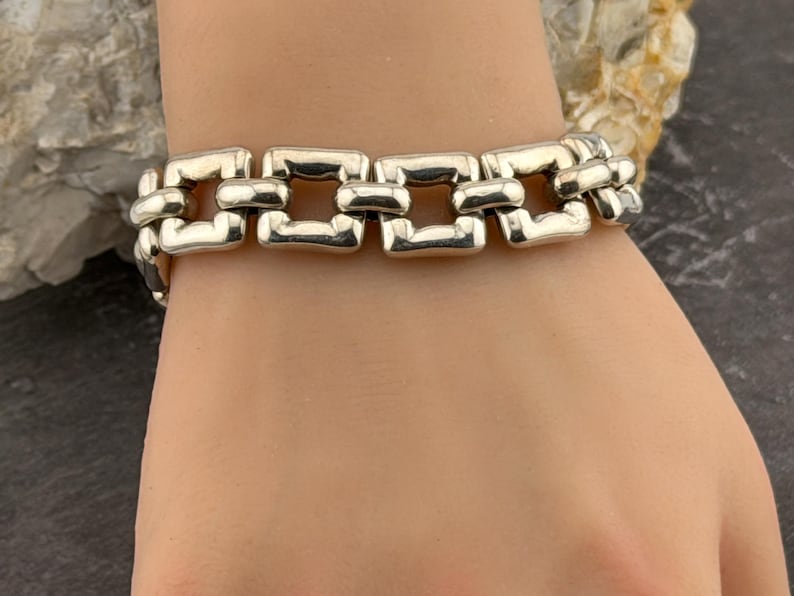 May include: A silver bracelet featuring a series of rectangular links. The bracelet is displayed on a wrist, highlighting its design and metallic shine. The links are connected, creating a flexible chain. The bracelet is a piece of jewellery.