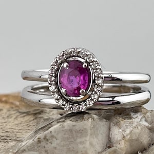 May include: A silver ring set with a pink oval gemstone surrounded by a halo of smaller white gemstones.