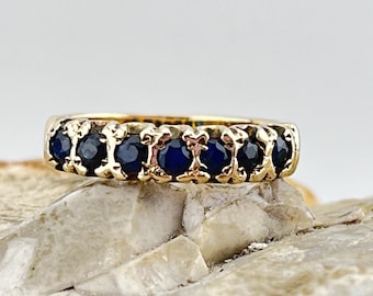 May include: A gold band ring with a row of dark blue sapphires.