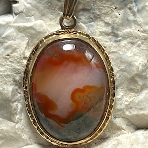 May include: A gold oval pendant featuring a brown, white and grey agate stone.