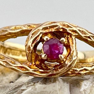 May include: A gold ring with a textured, twisted band and a single ruby gemstone in the center.