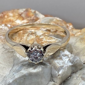 May include: A gold ring with a single, clear diamond set in a prong setting. The ring has a delicate, curved band with a wing-like design on each side of the diamond.