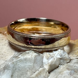 May include: A gold wedding band with a beaded edge.