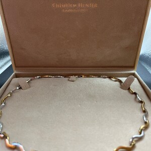 Op de afbeelding: Een gouden, zilveren en ros&eacute;gouden ketting met een golvend ontwerp. De ketting zit in een doos met de tekst "Chisholm Hunter Established 1857".