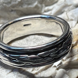 Könnte beinhalten: Ein silberner Ring mit geflochtenem Design. Der Ring besteht aus einem einzigen Metallband, das verdreht und geflochten ist, um eine strukturierte Oberfläche zu schaffen.
