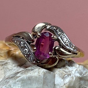 Puede incluir: Un anillo de oro con una piedra ovalada rosa y pequeños diamantes engastados en la banda.