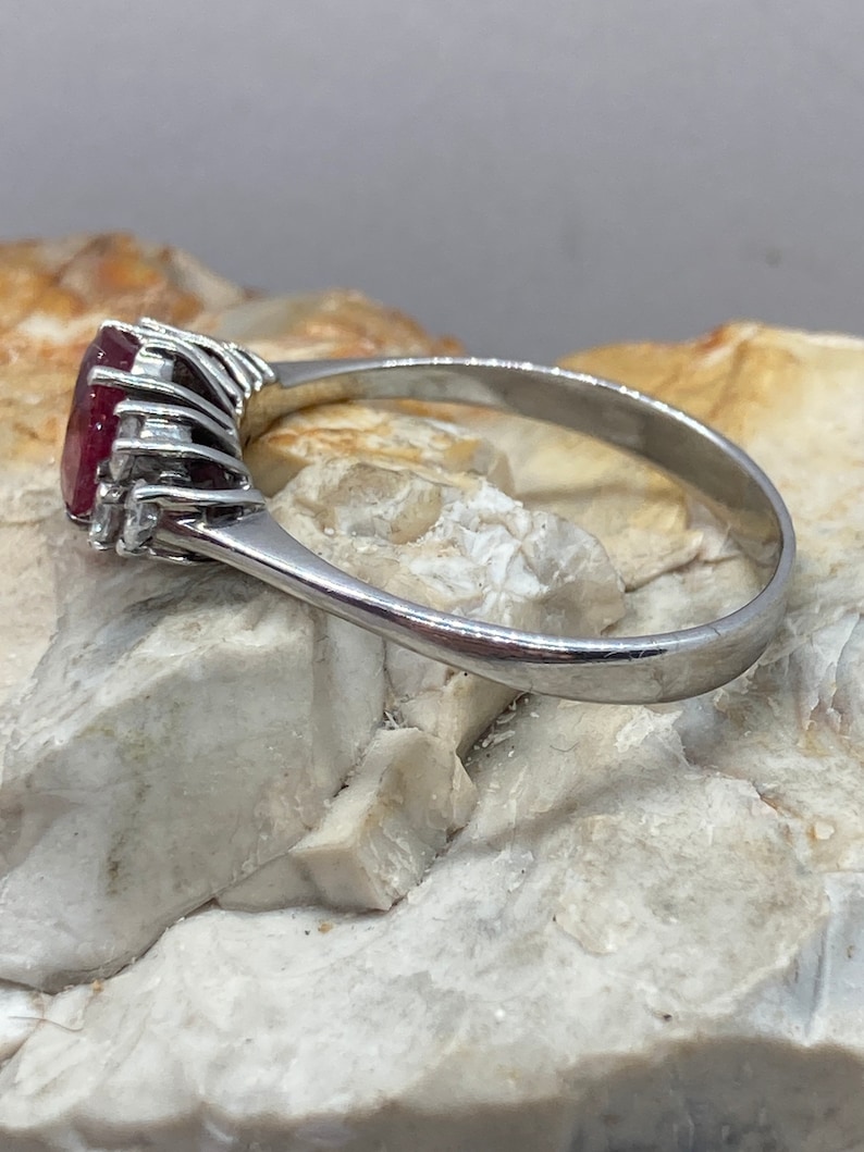 May include: A silver ring with a large, oval-shaped ruby gemstone surrounded by smaller diamonds. The ring is set on a white background.