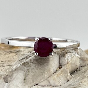 May include: A simple silver band ring with a single round ruby gemstone in the center.