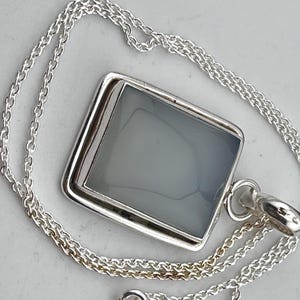 May include: A silver chain necklace with a square pendant featuring a gray stone.