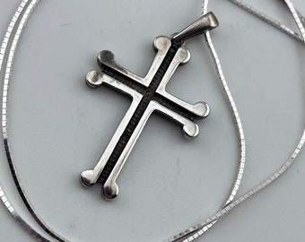 Puede incluir: Un collar de cadena de plata con un colgante de cruz de plata. La cruz tiene un diseño detallado con múltiples puntos.