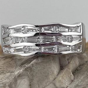 May include: A silver band ring with a wavy design and multiple rows of baguette-cut clear stones.