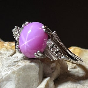 Op de afbeelding: Een zilveren ring met een grote roze ster-saffier edelsteen en kleinere diamanten die in de band zijn gezet.
