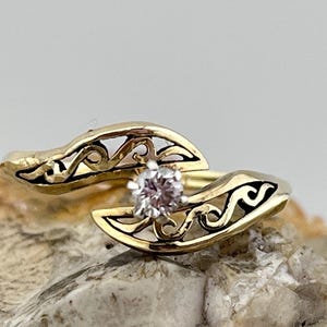 May include: A gold ring with a delicate, intricate design featuring a single, clear diamond in the center.