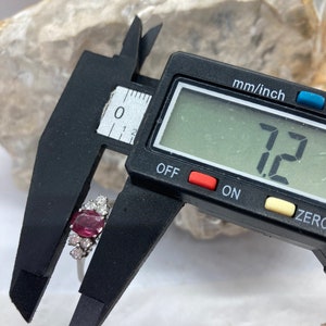 May include: Close-up of a ring with a large, oval-shaped, pink gemstone surrounded by smaller, white gemstones. The ring is being measured with a digital caliper, which reads "7.2".