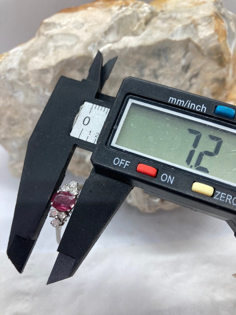 May include: Close-up of a ring with a large, oval-shaped, pink gemstone surrounded by smaller, white gemstones. The ring is being measured with a digital caliper, which reads "7.2".