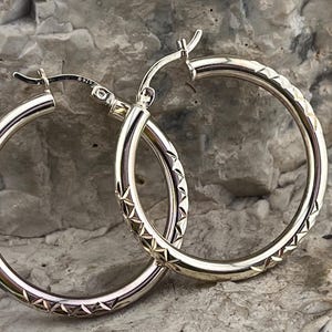 May include: Silver hoop earrings with a geometric pattern on the outer edge.