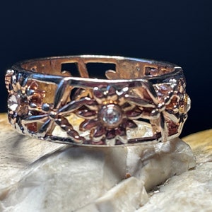 Puede incluir: Un anillo de plata con un delicado diseño floral y una piedra transparente en el centro.