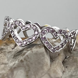 Puede incluir: Un anillo de plata con un diseño de cuatro corazones entrelazados, cada corazón está engastado con pequeñas piedras rosas.