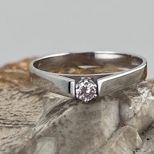 May include: A simple silver band ring with a single, small, round, clear gemstone in the centre.