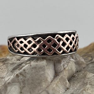 May include: A silver ring with a rose gold Celtic knot design.