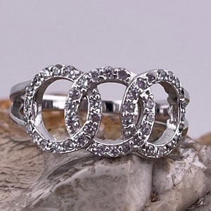May include: A silver ring featuring three interlocked circles, each circle is set with small clear stones.
