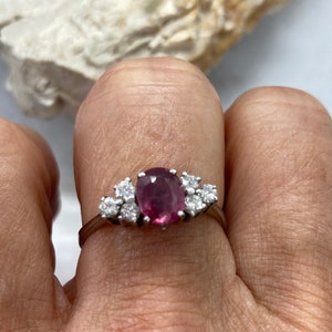 May include: A silver ring with a pink oval gemstone surrounded by smaller clear gemstones.