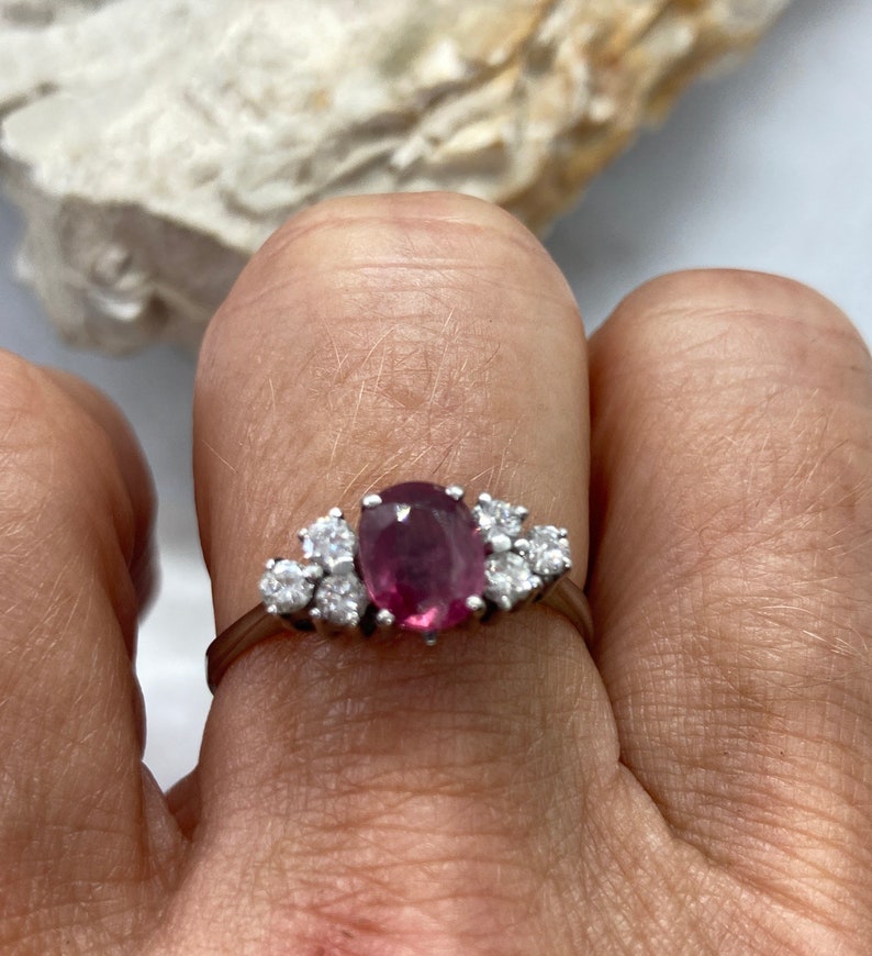 May include: A silver ring with a pink oval gemstone surrounded by smaller clear gemstones.
