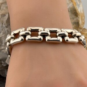 May include: A silver bracelet featuring a chain link design. The bracelet is made up of rectangular links, giving it a bold, contemporary look. The links are joined to create a continuous band, suitable for wrist wear.