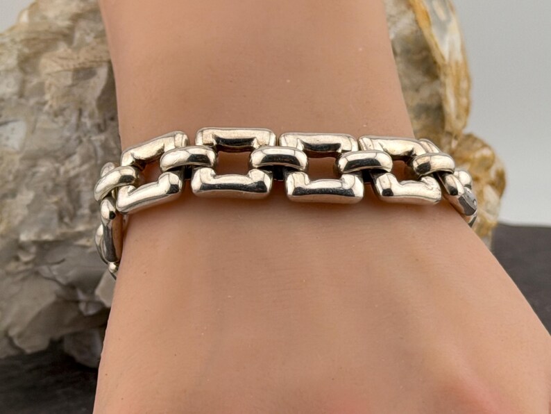 May include: A silver bracelet featuring a chain link design. The bracelet is made up of rectangular links, giving it a bold, contemporary look. The links are joined to create a continuous band, suitable for wrist wear.